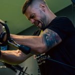 Muscular man with tattoos exercising on a cable machine in a gym, showcasing strength and determination.